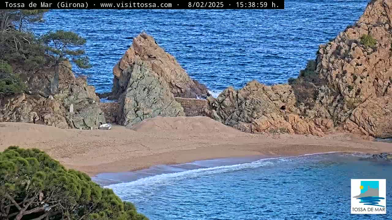 A secluded sandy cove nestled between rocky cliffs meets a calm blue sea under a clear sky.