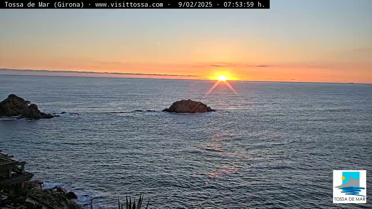A sunset over a calm ocean with two rocky outcrops visible in the foreground.