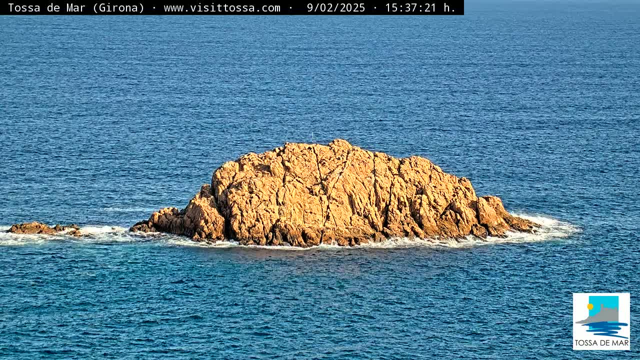 A tan-colored rocky island sits in a calm, blue ocean.