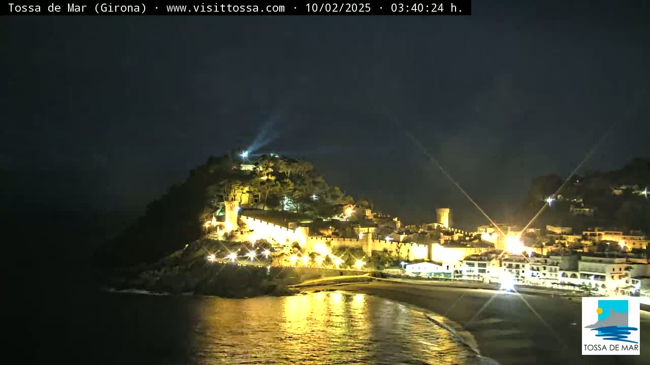 A hilltop town, illuminated at night, overlooks a dark, calm ocean.
