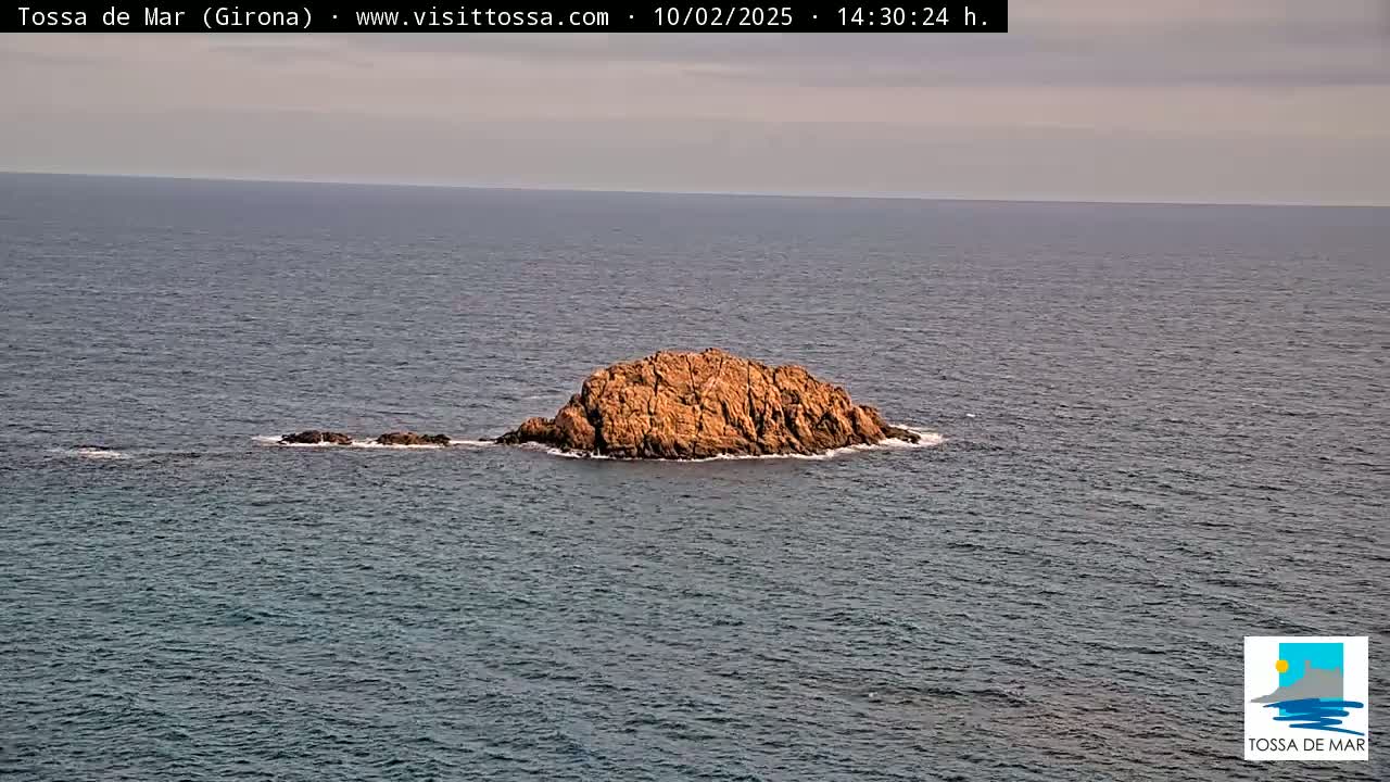 A small, rocky island sits in the calm, dark-blue ocean under a mostly cloudy sky.