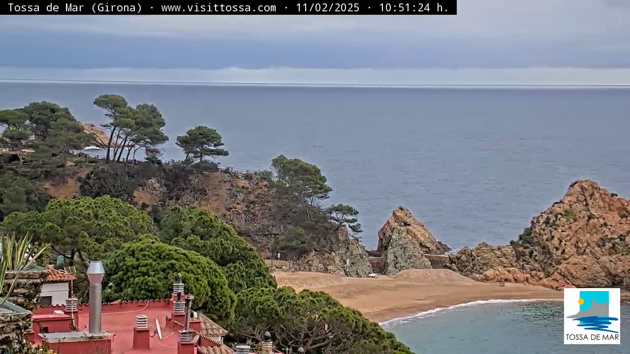 A mostly cloudy day reveals a coastal scene with a sandy cove nestled between rocky cliffs, overlooking a calm sea dotted with evergreen trees.