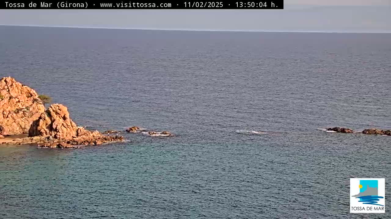 A rocky outcrop juts into a calm, blue-gray sea under a clear sky.