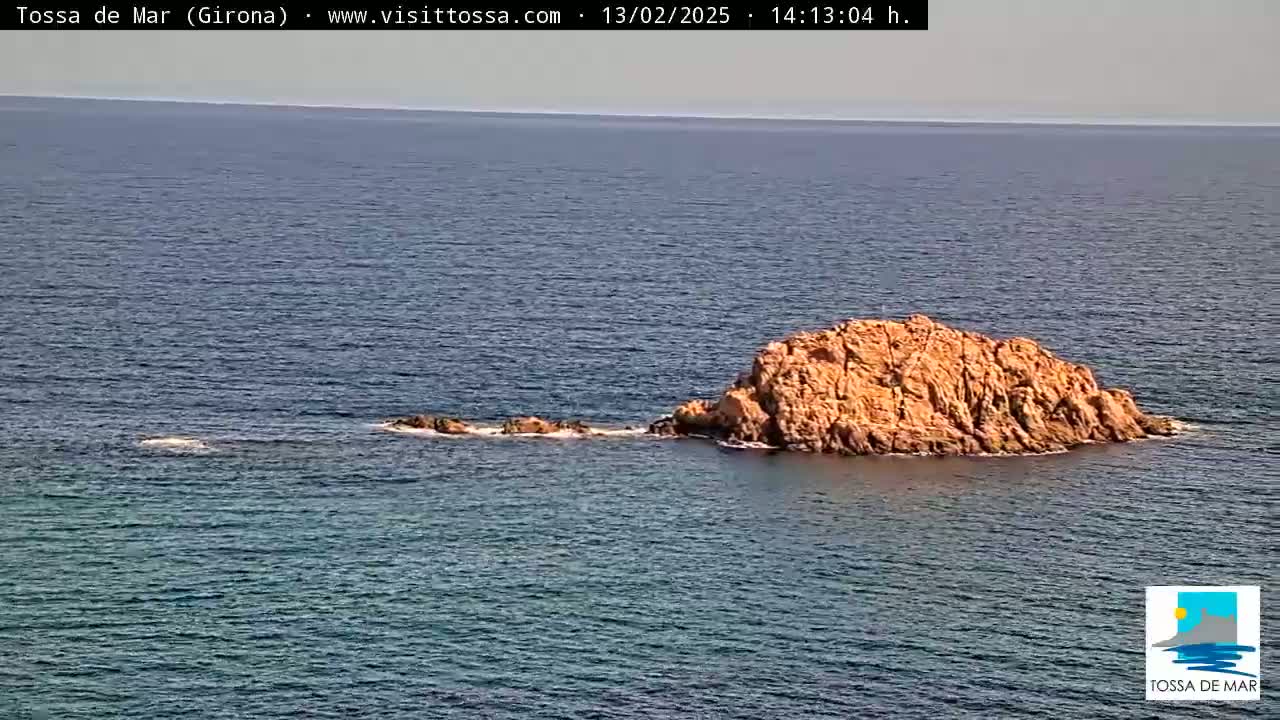 A rocky islet sits in a calm, blue sea under a clear sky.