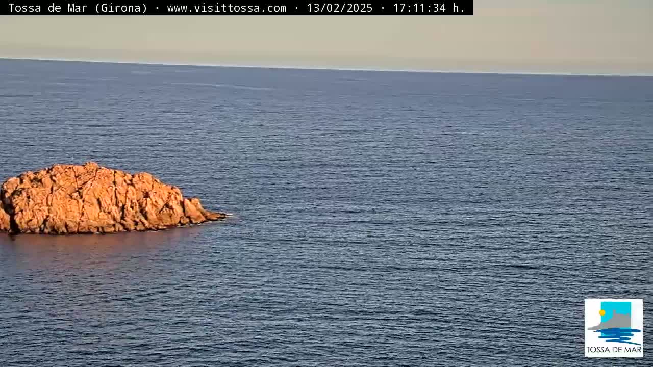 A rocky islet sits in a calm, blue sea under a pale sky.