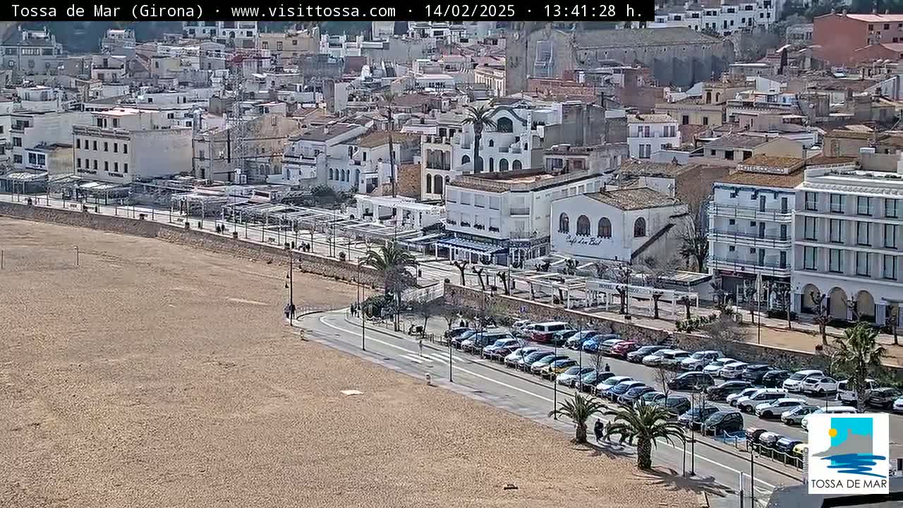 A sandy beach and a seaside town with parked cars and buildings under a sunny sky.