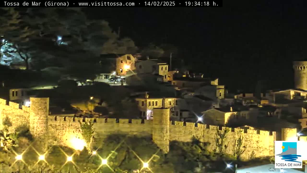 A nighttime view of a stone walled town illuminated by artificial lights.