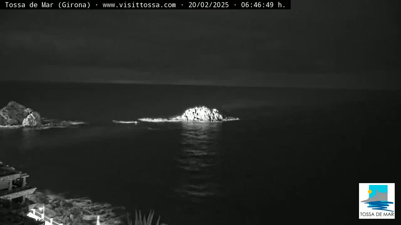 A nighttime, grayscale image shows two rocky outcroppings in the dark ocean with calm water.