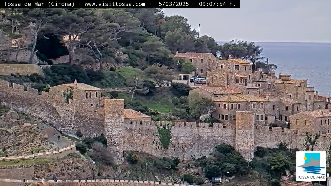 A stone walled village overlooks a calm sea under an overcast sky.