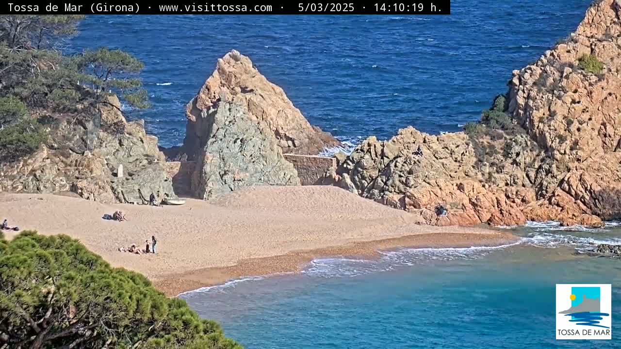 A sandy beach nestled between rocky cliffs meets a calm, blue ocean under a sunny sky.