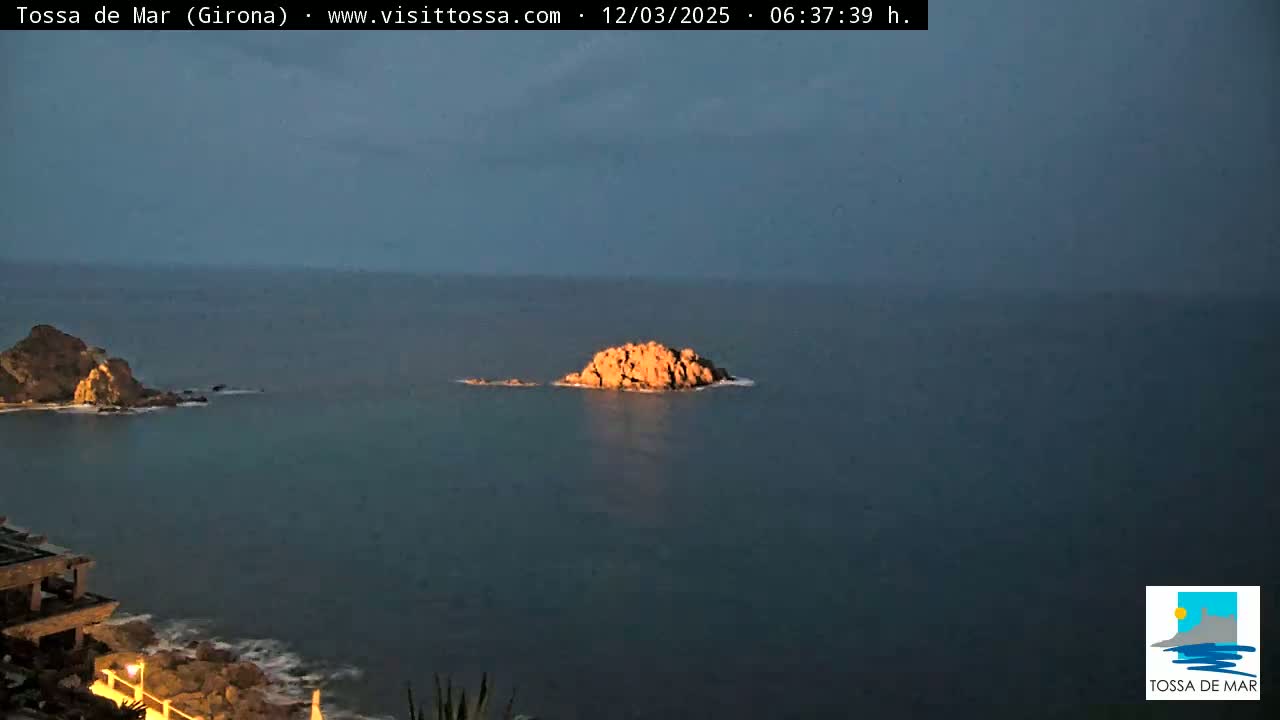 A rocky islet sits in calm, dark-blue water at twilight, with a larger landmass visible in the distance.