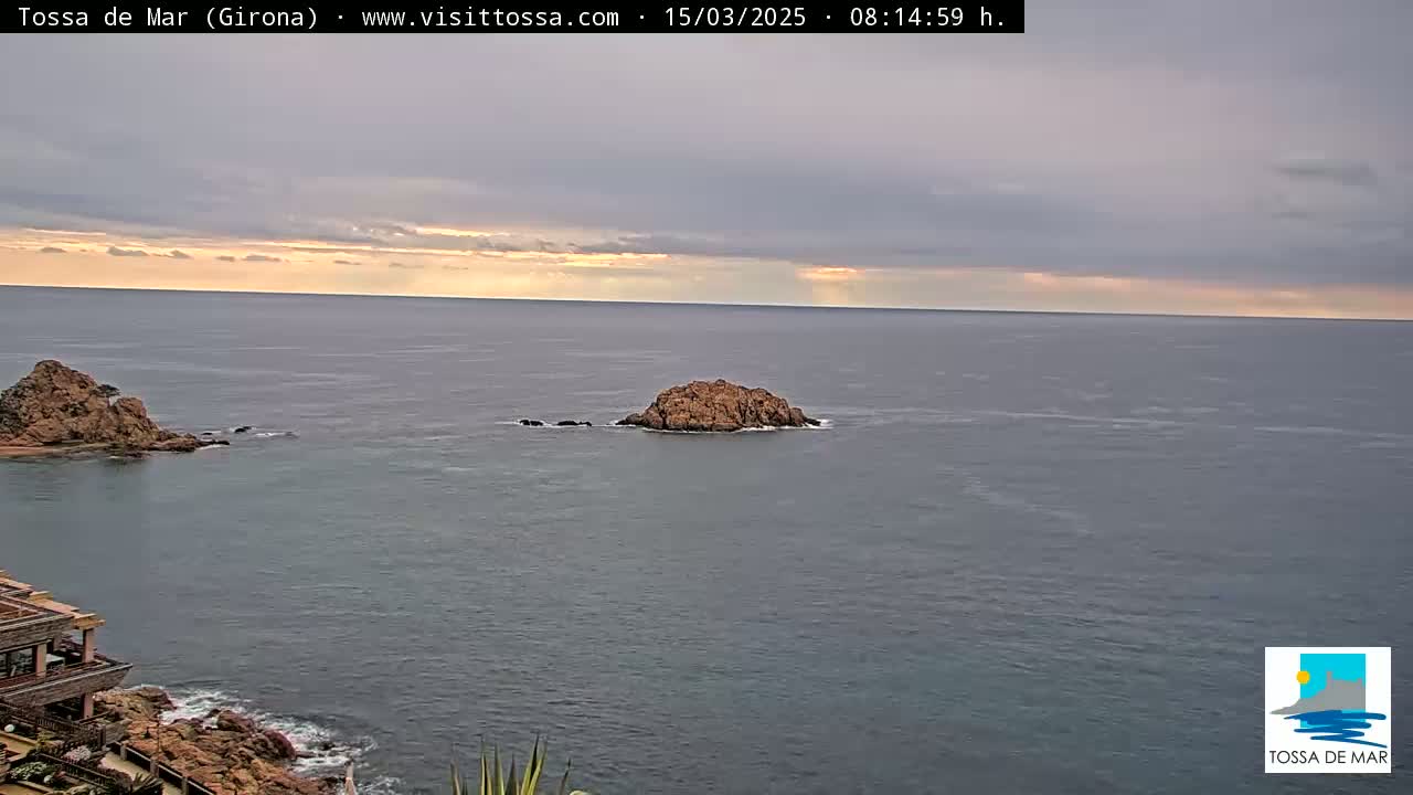 Two rocky outcroppings are visible in a calm sea under a partly cloudy, dusky sky.