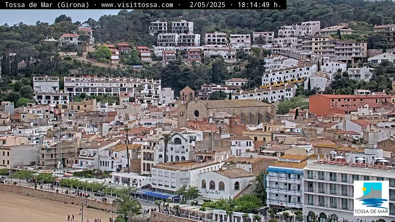 A coastal town with numerous white buildings, a church, and a sandy beach is visible under a mostly clear sky.