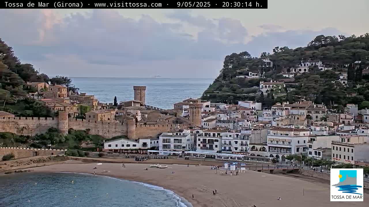A coastal town with a medieval wall and sandy beach is visible under a partly cloudy sky.