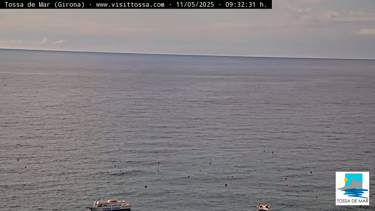 A calm sea with a few small boats and scattered buoys under a mostly cloudy sky.