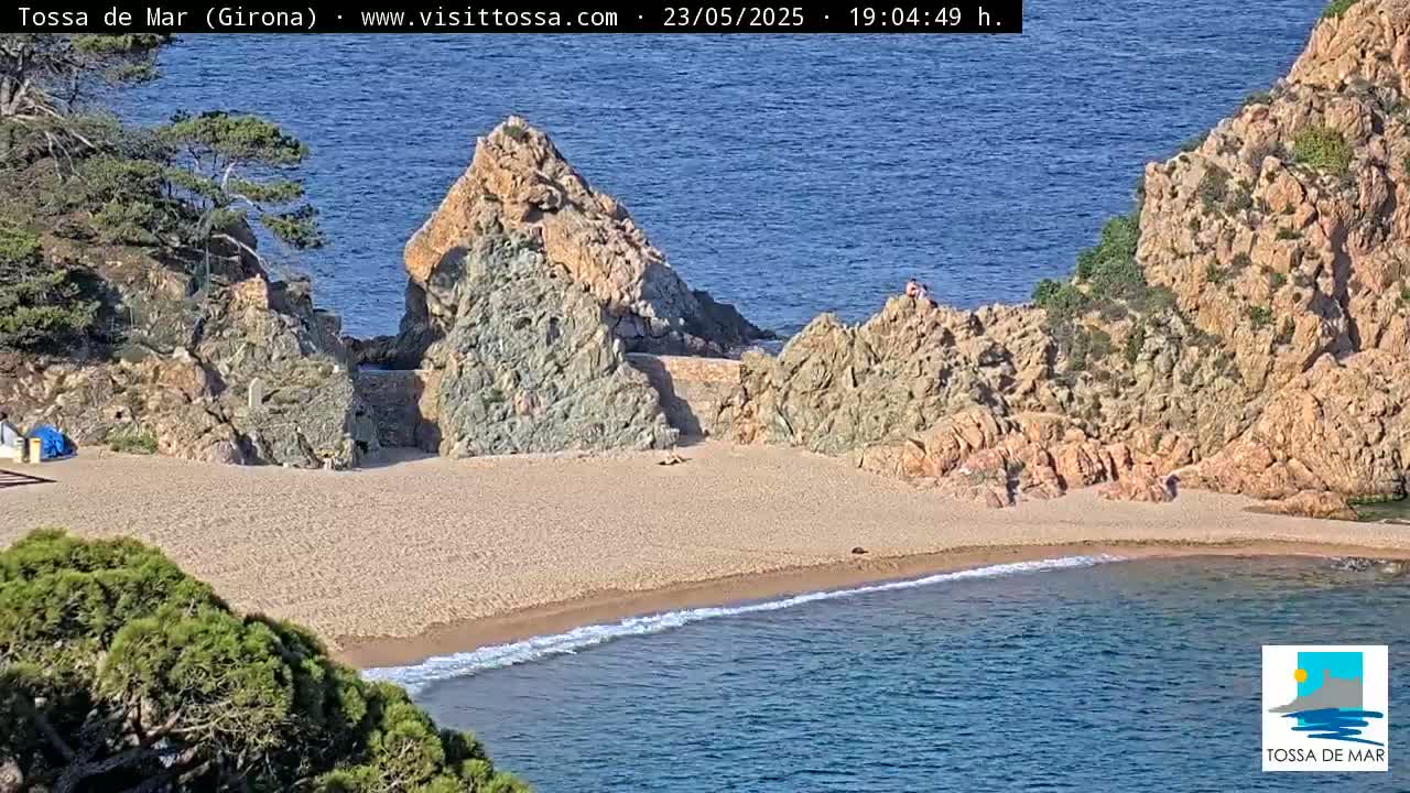 A sandy cove nestled between rocky cliffs, with calm blue water lapping at the shore on a sunny day.