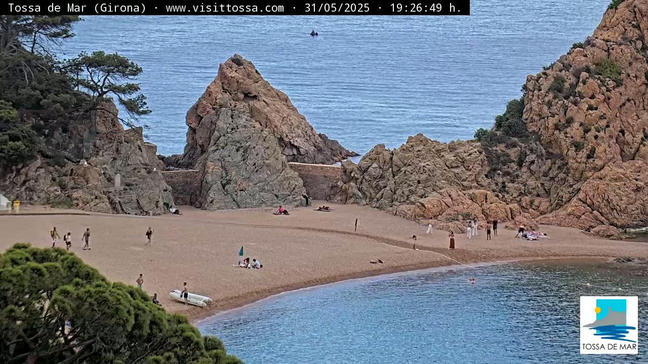 A sandy cove nestled between rocky cliffs, with a calm sea and several people relaxing on the beach.