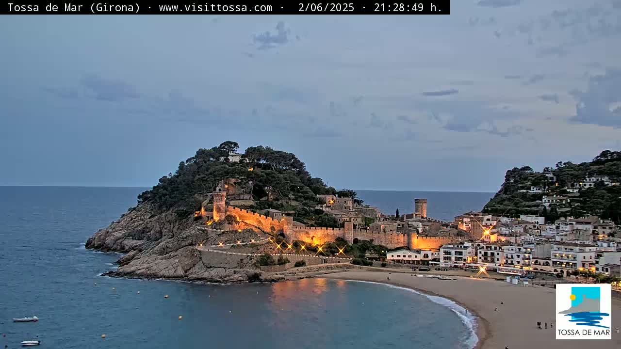 A coastal town with a medieval castle on a hill overlooking a calm bay at dusk.