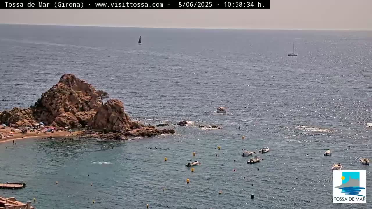 A rocky outcrop with a small beach and several small boats in calm, sunny waters.