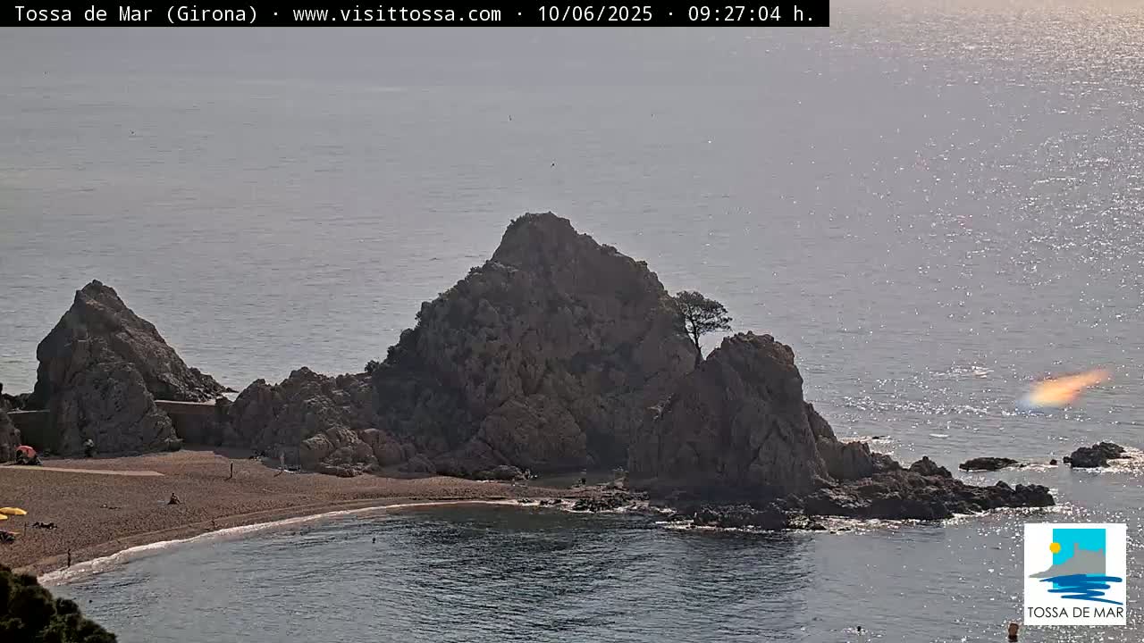 A rocky, triangular peninsula juts into a calm, hazy sea, with a small sandy beach nestled at its base.