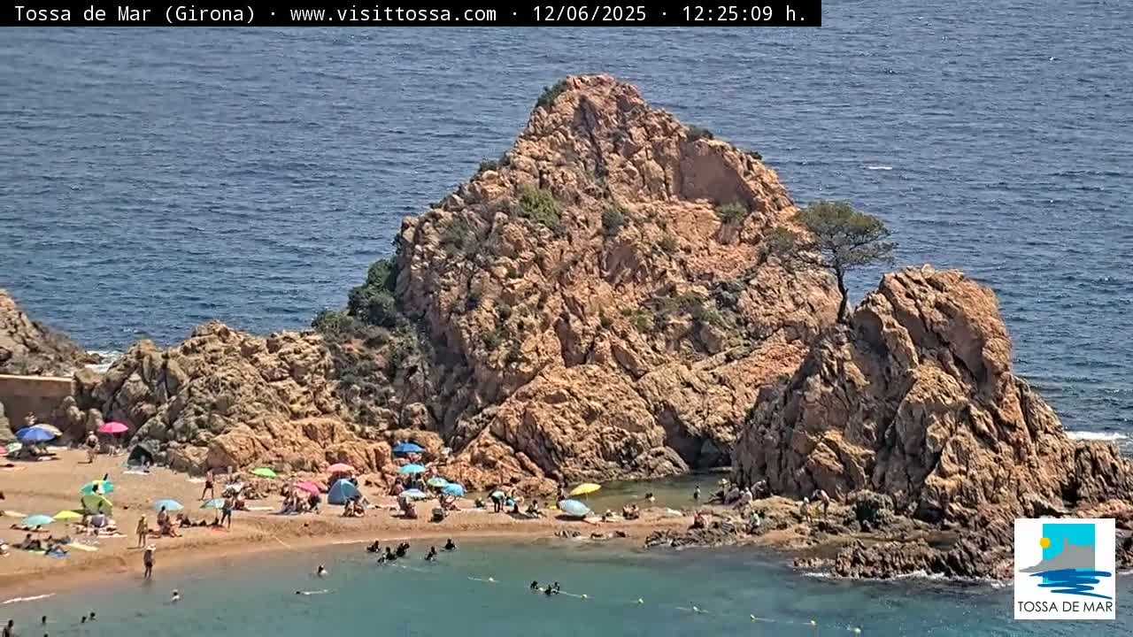 A rocky cove with a sandy beach, populated by sunbathers under colorful umbrellas, sits beside a calm blue sea under a sunny sky.