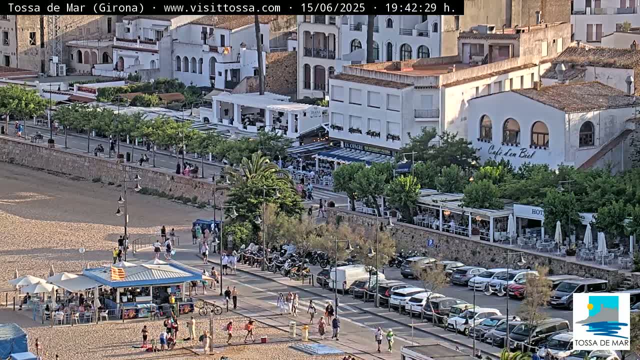 A beachside town with restaurants, parked cars, and pedestrians, under a sunny sky.
