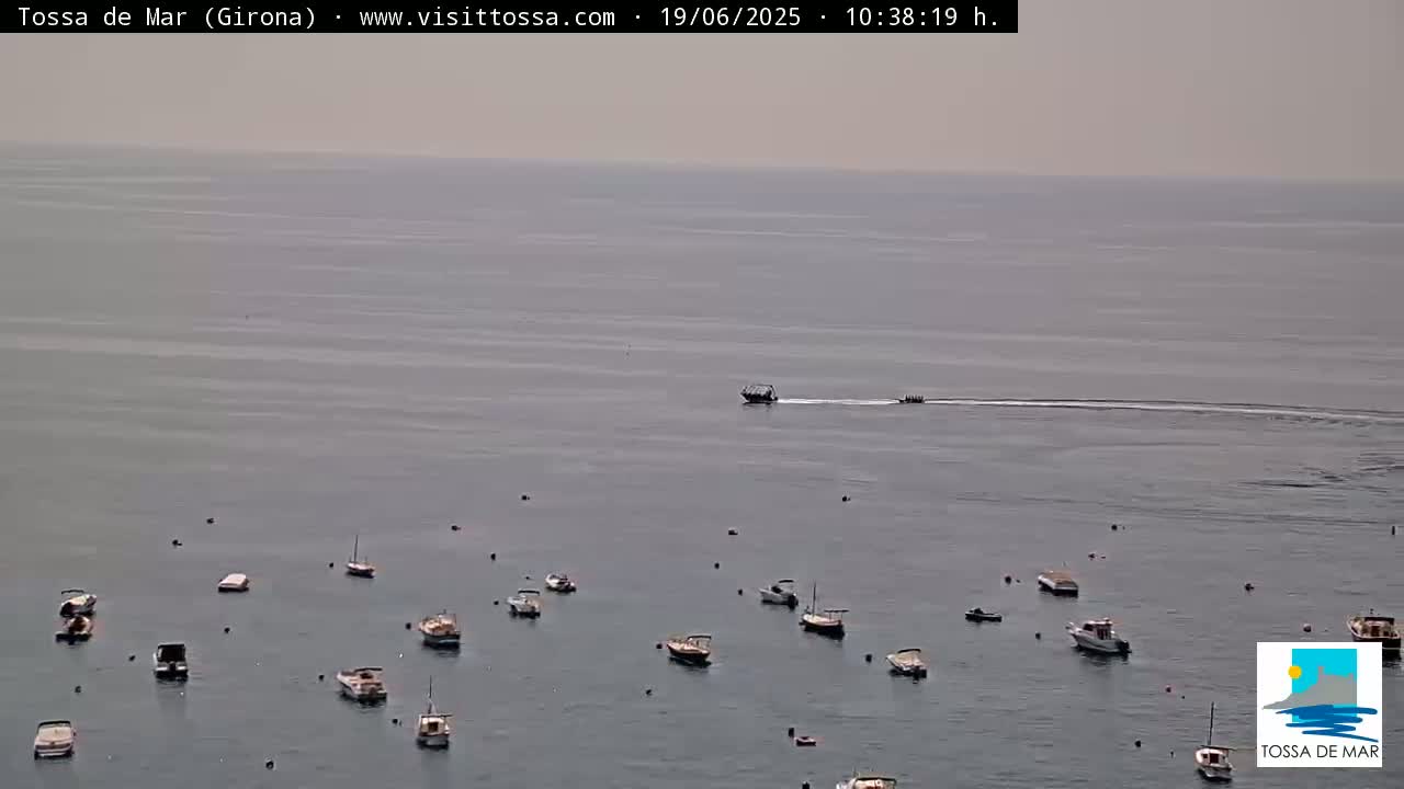 Numerous small boats are anchored in a calm, hazy sea, with a larger boat and a smaller vessel traveling further out.