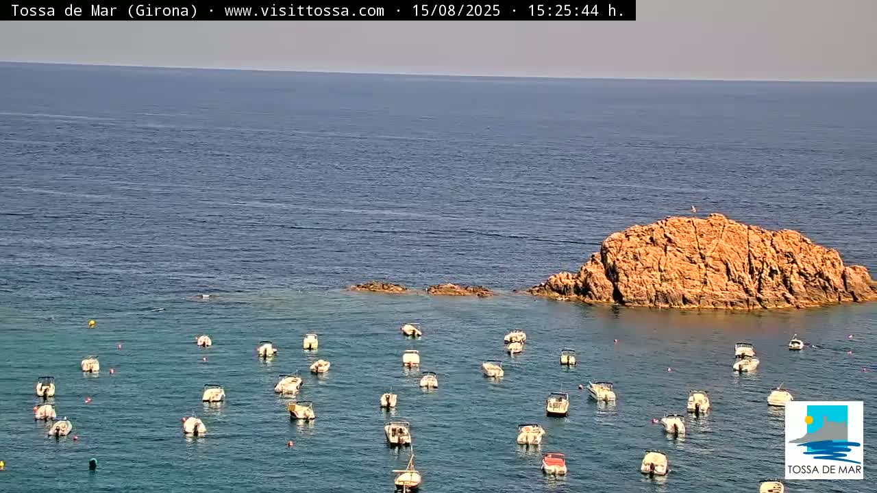 Numerous small boats are anchored in a calm, light-blue sea under a hazy sky.