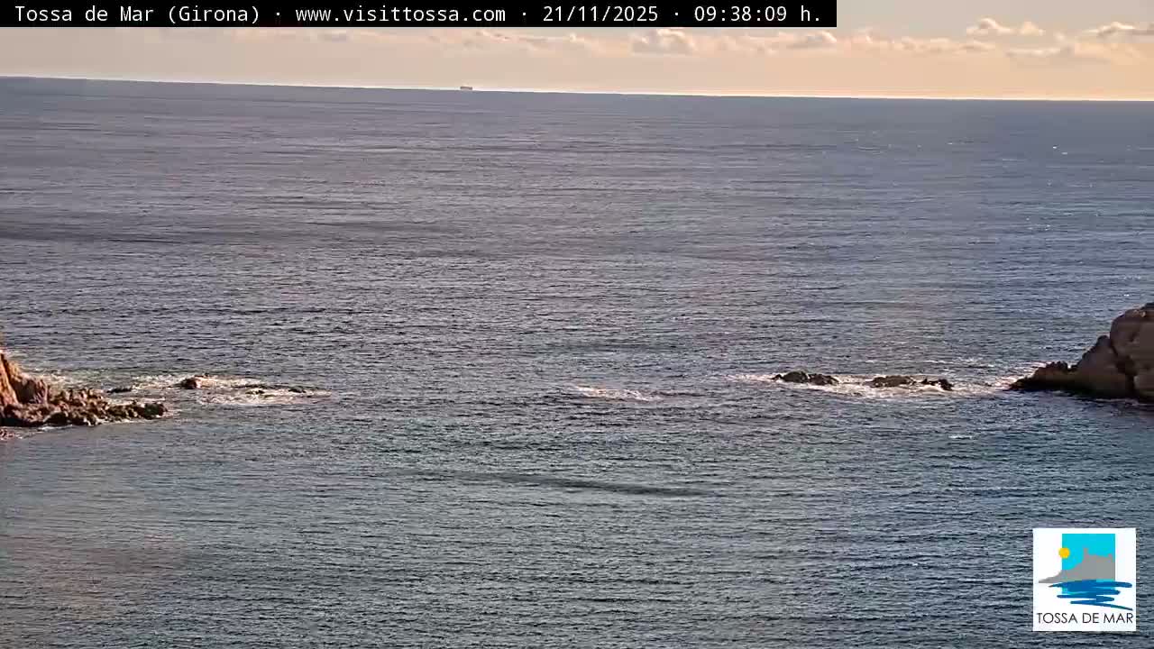 A vast expanse of calm blue-grey sea with rocky outcrops on the left and right, and a distant ship visible on the horizon, all under a partly cloudy sky.