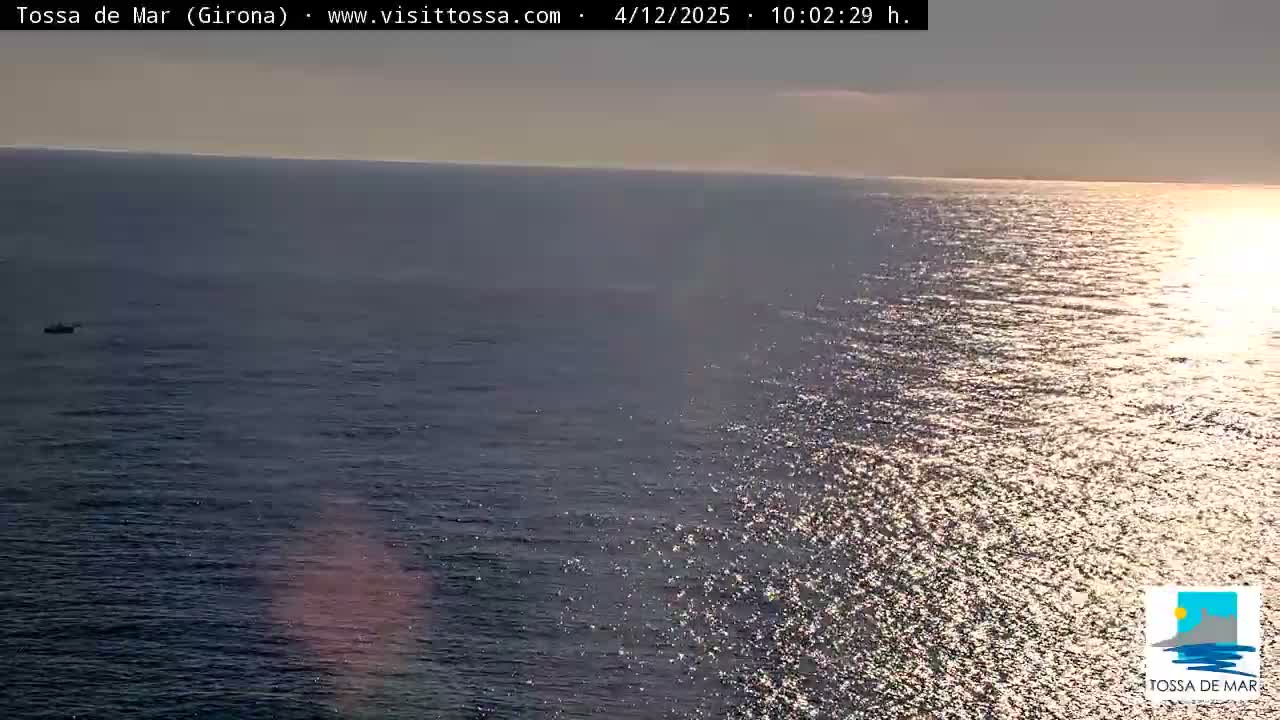 A small boat floats on calm ocean waters under a clear and bright sky, with intense morning sunlight shimmering across the surface.