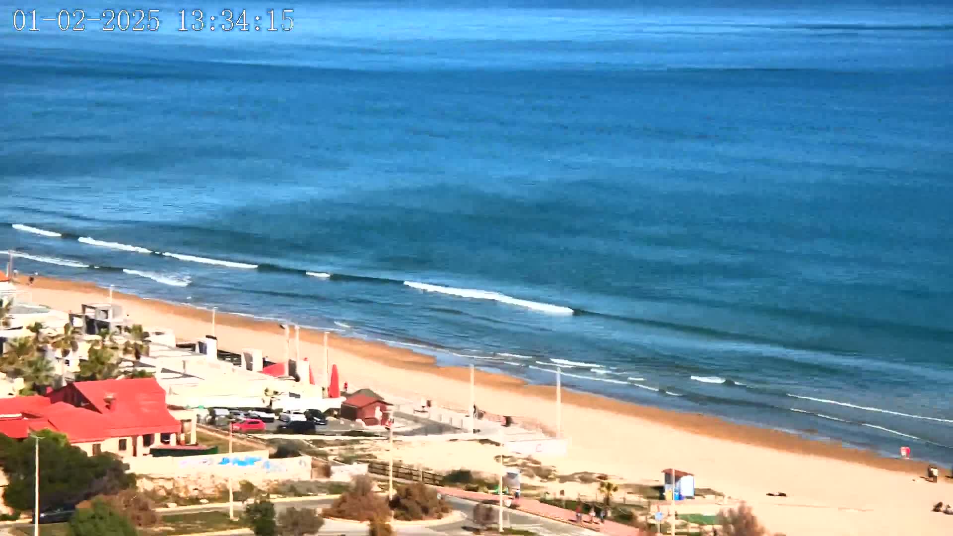 A sandy beach with small waves and buildings is visible under a clear sky.