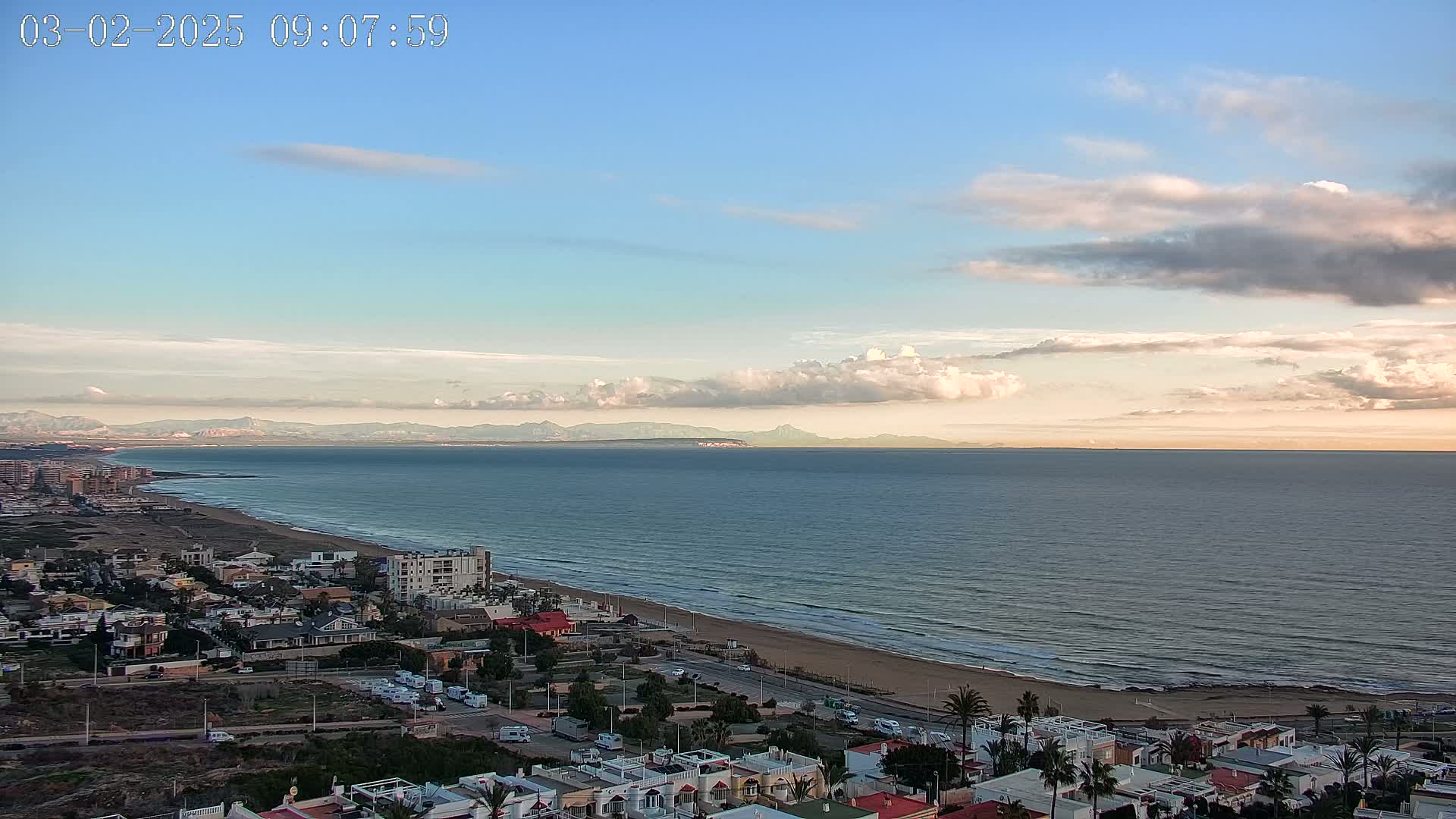 A coastal town overlooks a wide, calm ocean under a partly cloudy sky.