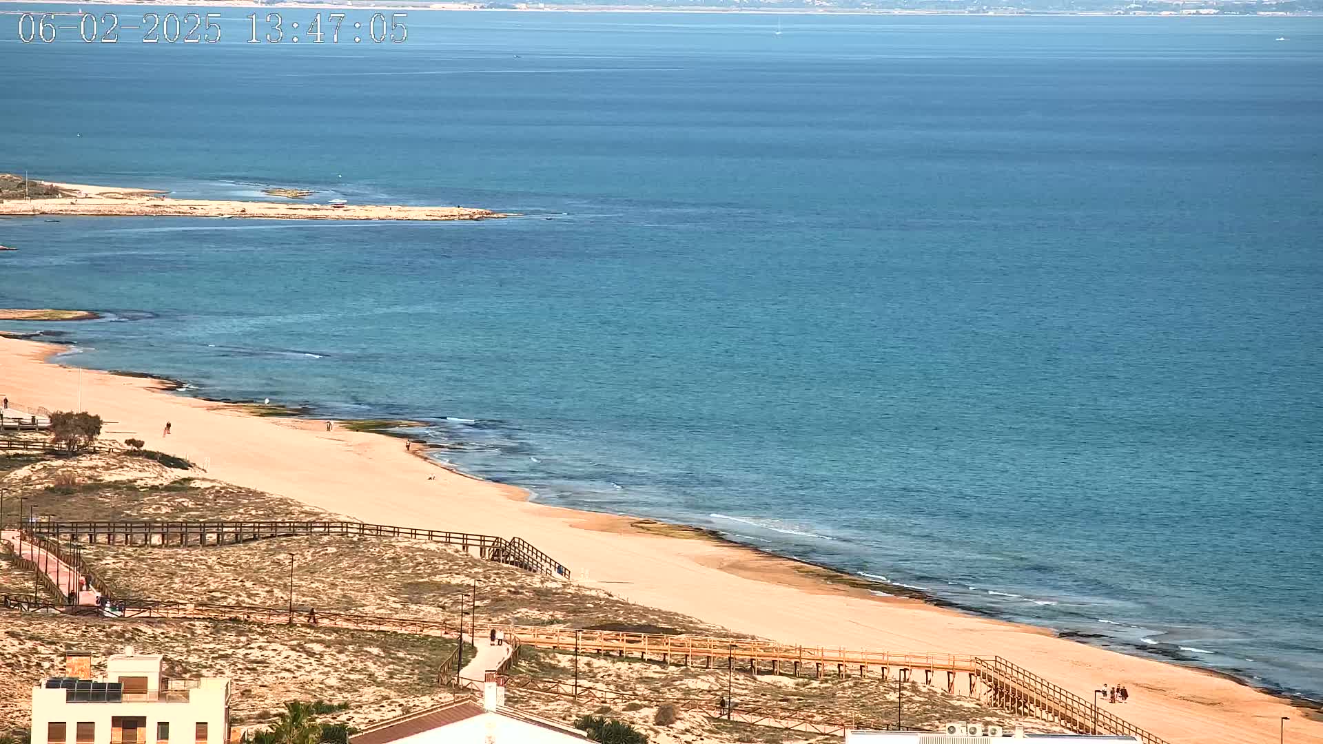 A sandy beach with wooden walkways stretches along a calm, blue ocean under a clear sky.