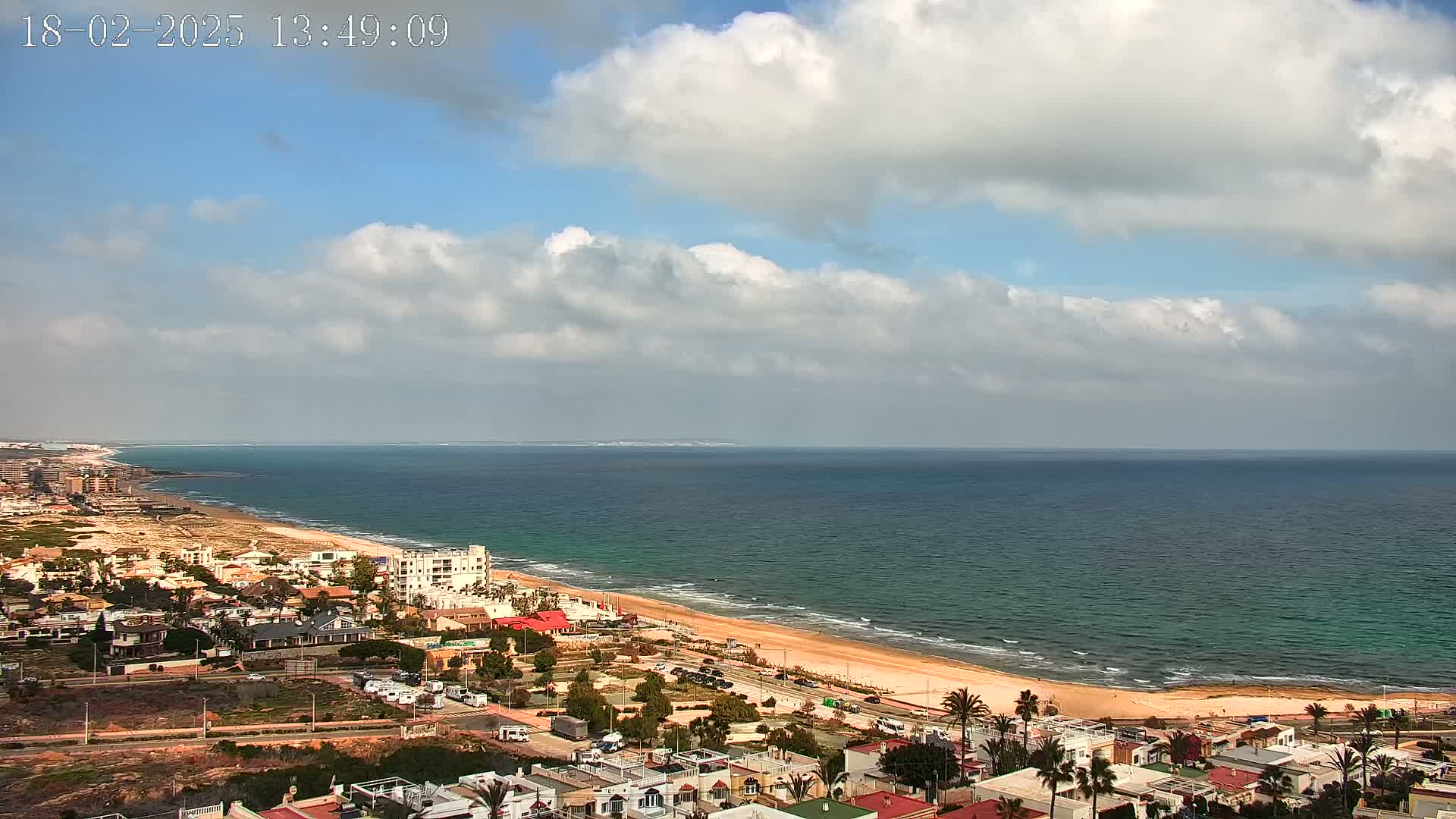 A coastal town with a sandy beach and calm ocean under a partly cloudy sky.