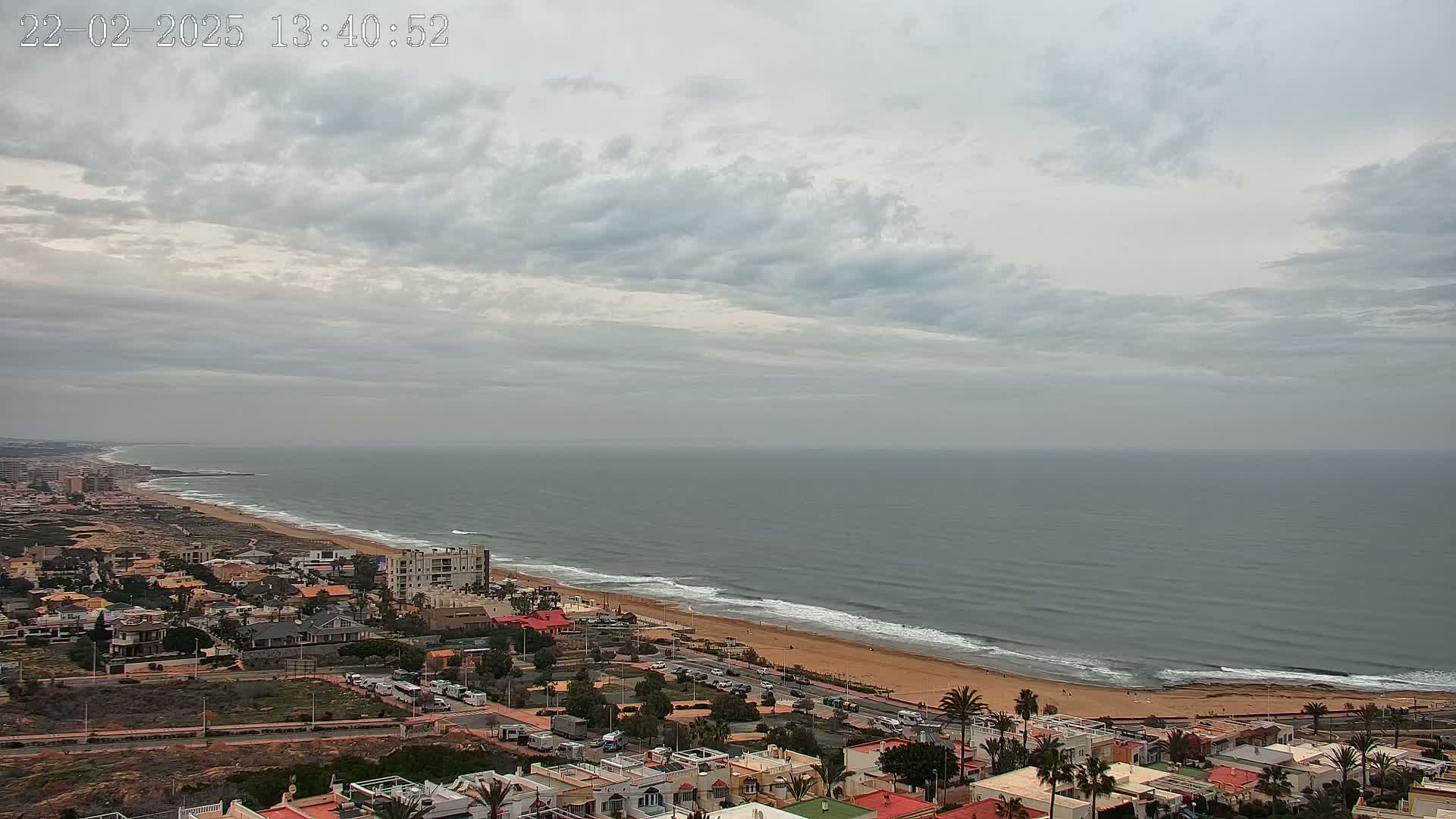 A coastal town with a sandy beach and calm ocean under a mostly cloudy sky.