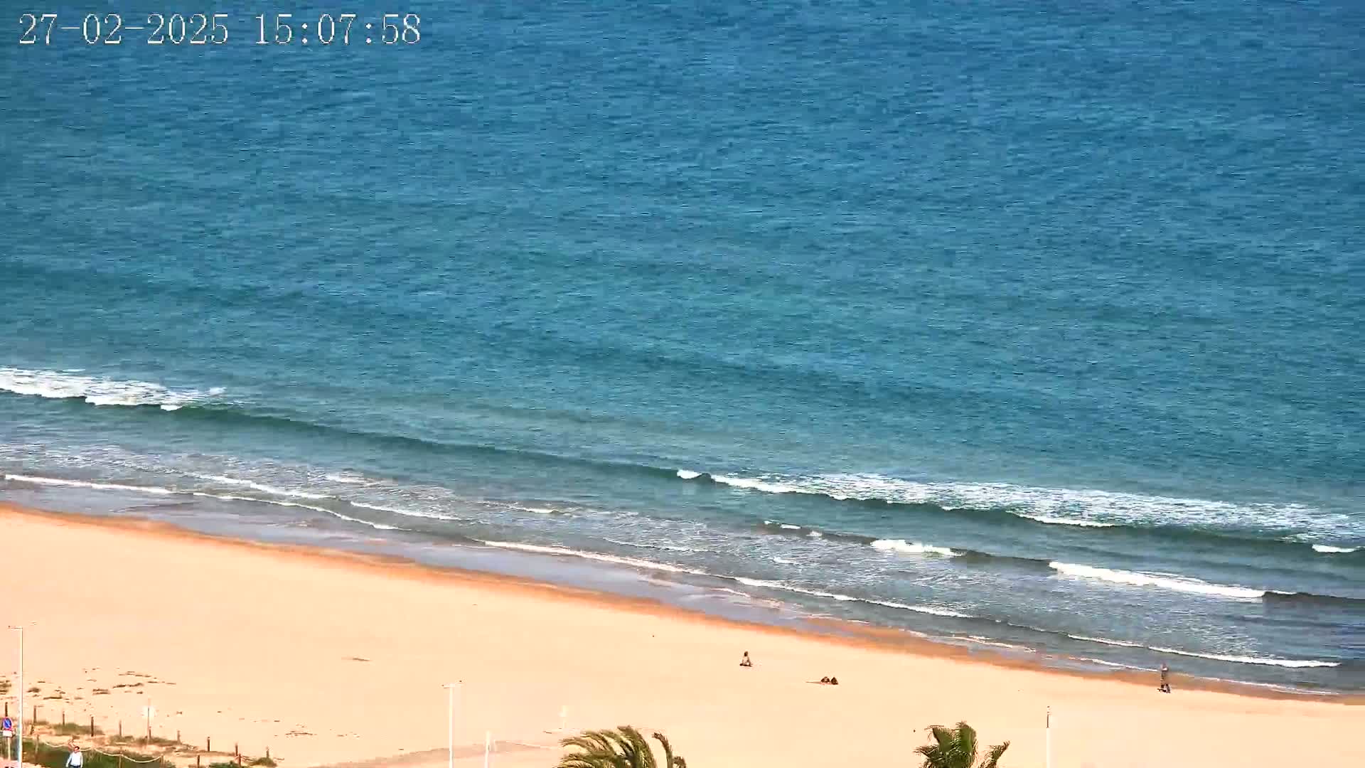 An expansive sandy beach meets a calm, blue ocean with gentle waves under a clear sky.
