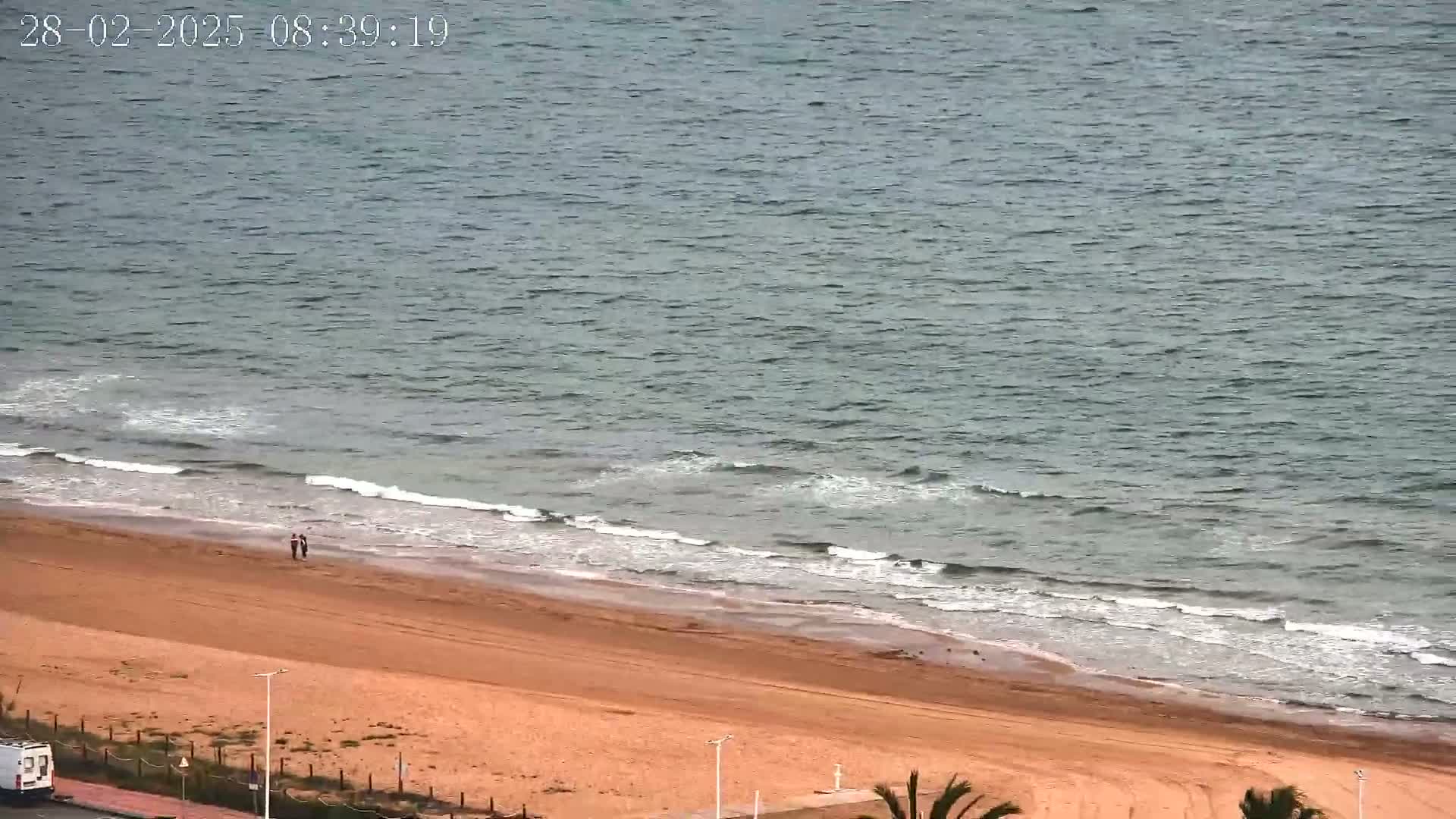 An expansive sandy beach meets a calm, gray-blue ocean under an overcast sky.