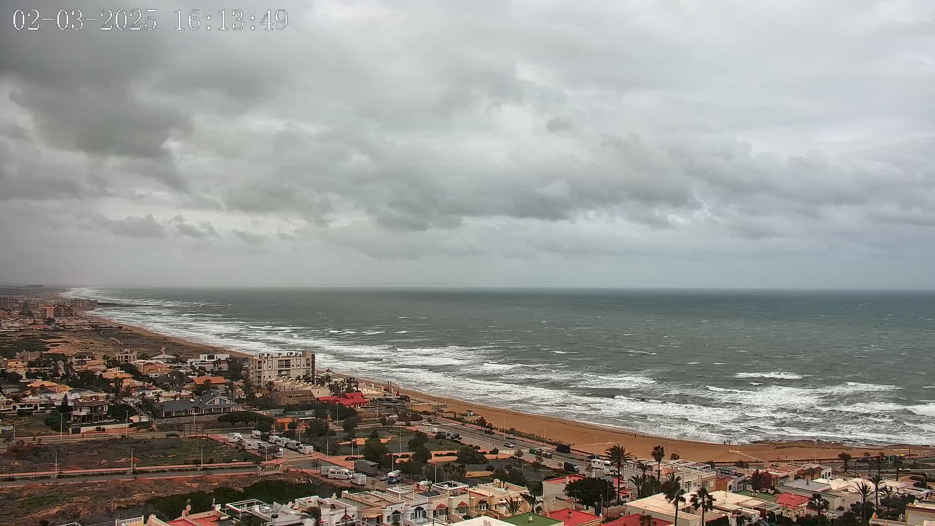 A coastal town overlooks a beach with a choppy sea under a cloudy sky.