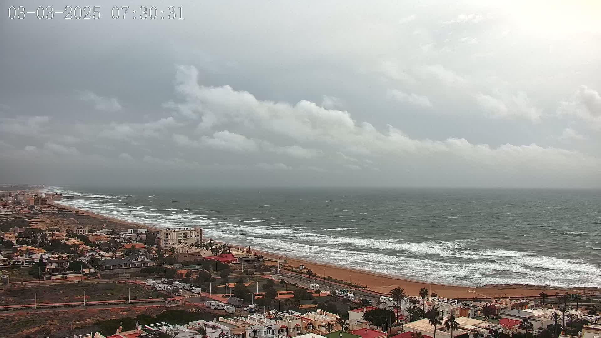 A coastal town overlooks a windy ocean with choppy waves under a cloudy sky.
