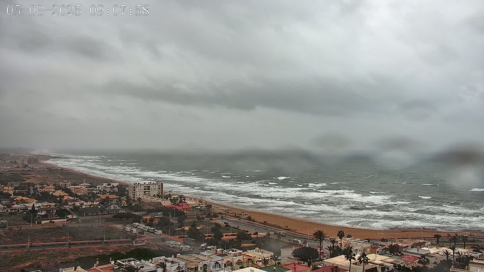 A coastal town is shown under an overcast sky with a choppy sea visible along a sandy beach.