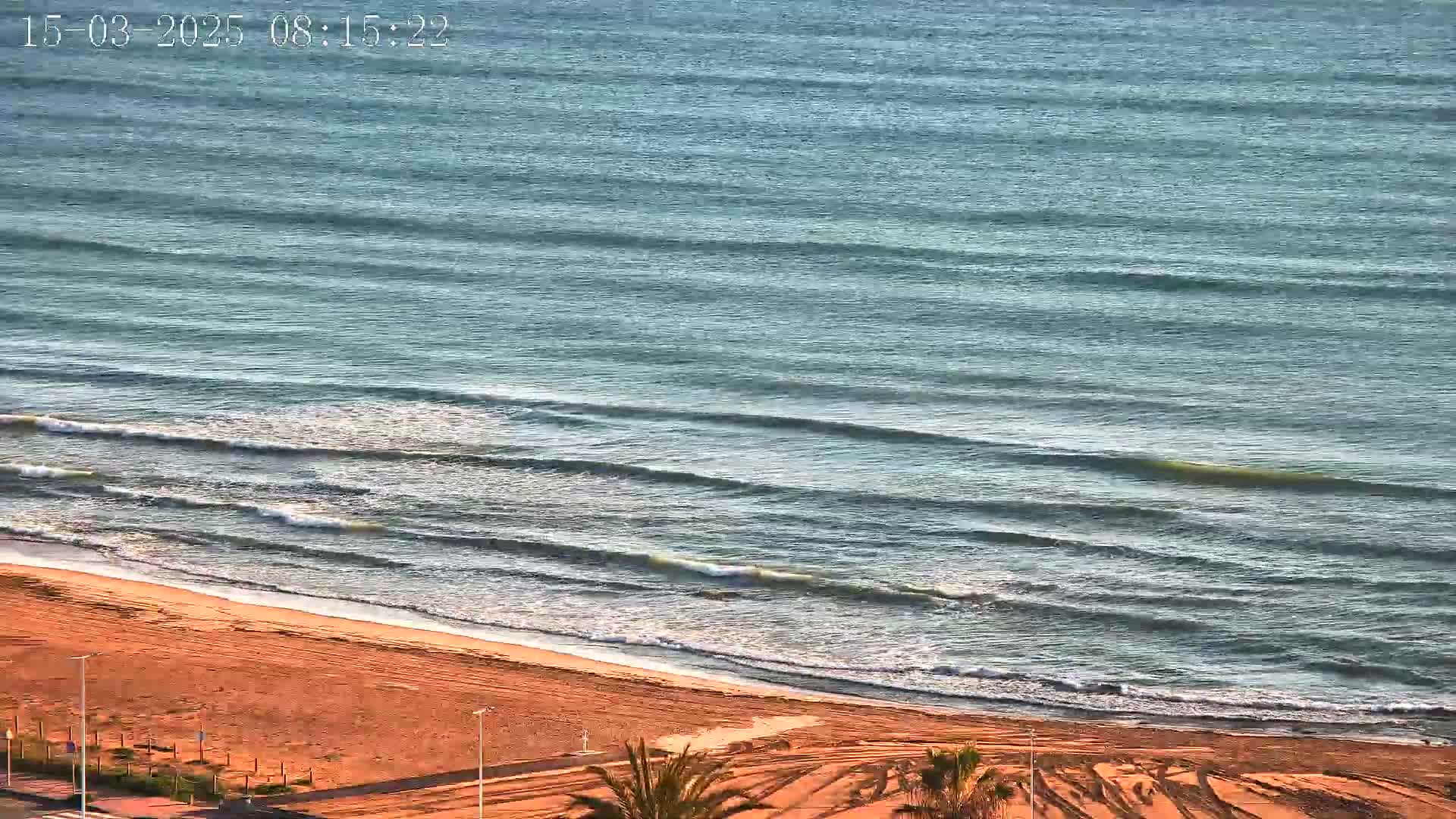A sandy beach meets a calm ocean with small waves under a clear sky.