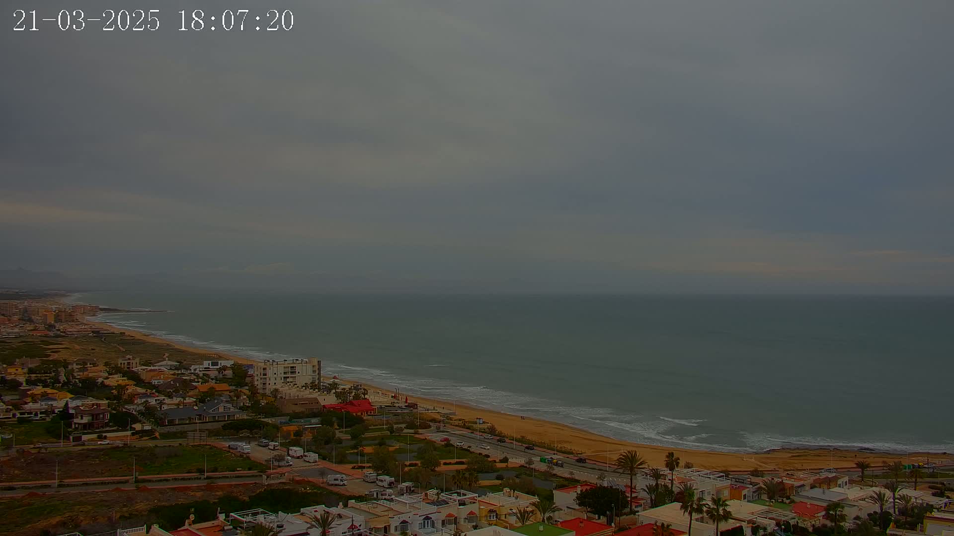 A coastal town overlooks a calm, gray ocean under an overcast sky.