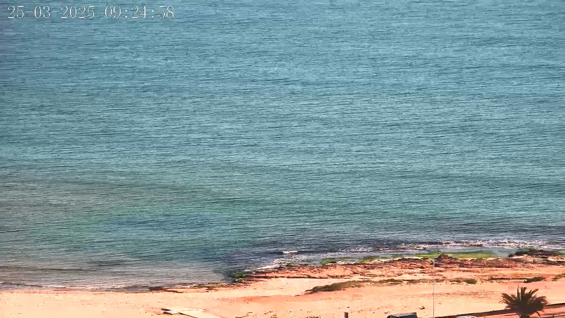 A sandy beach meets a calm, teal ocean under a clear sky.