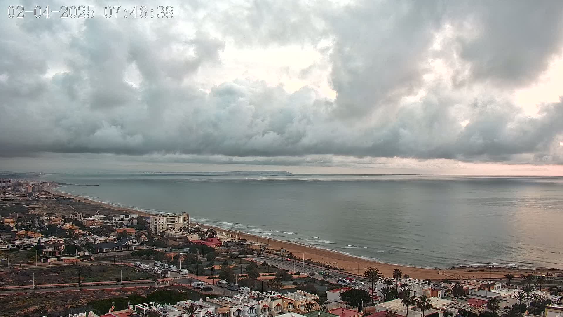 A coastal town overlooks a wide, grey ocean under a cloudy sky.