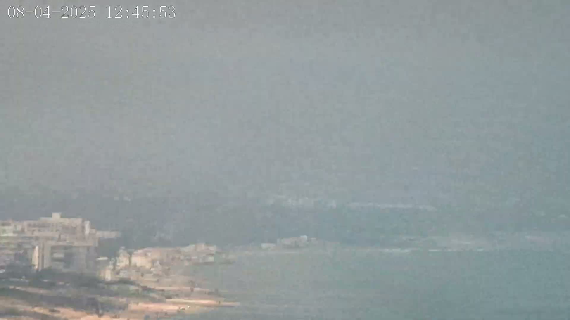 A hazy view shows a distant coastline with buildings and a body of water under a hazy sky.