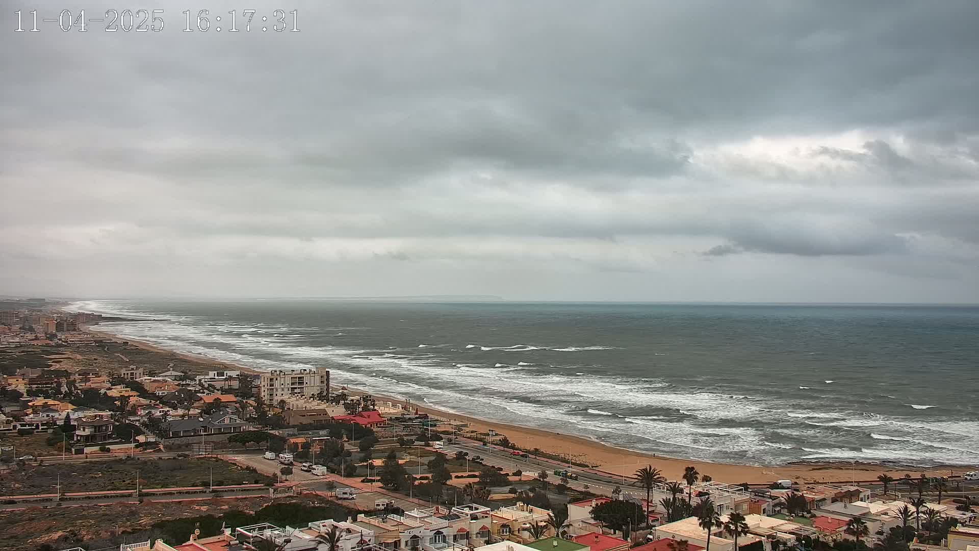 A coastal town overlooks a beach with moderate waves under an overcast sky.