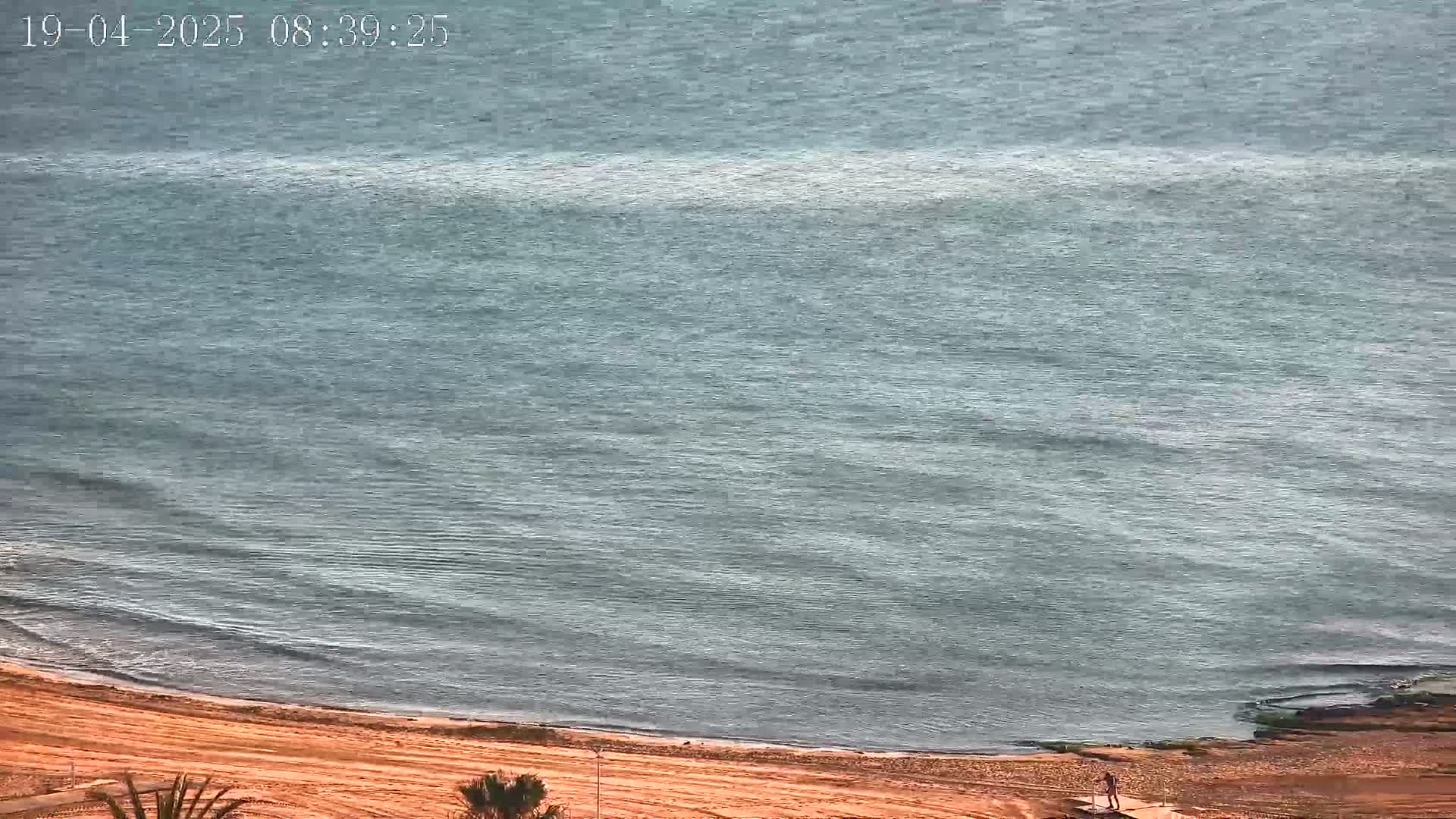 A calm, gray-blue sea laps gently onto a sandy beach.
