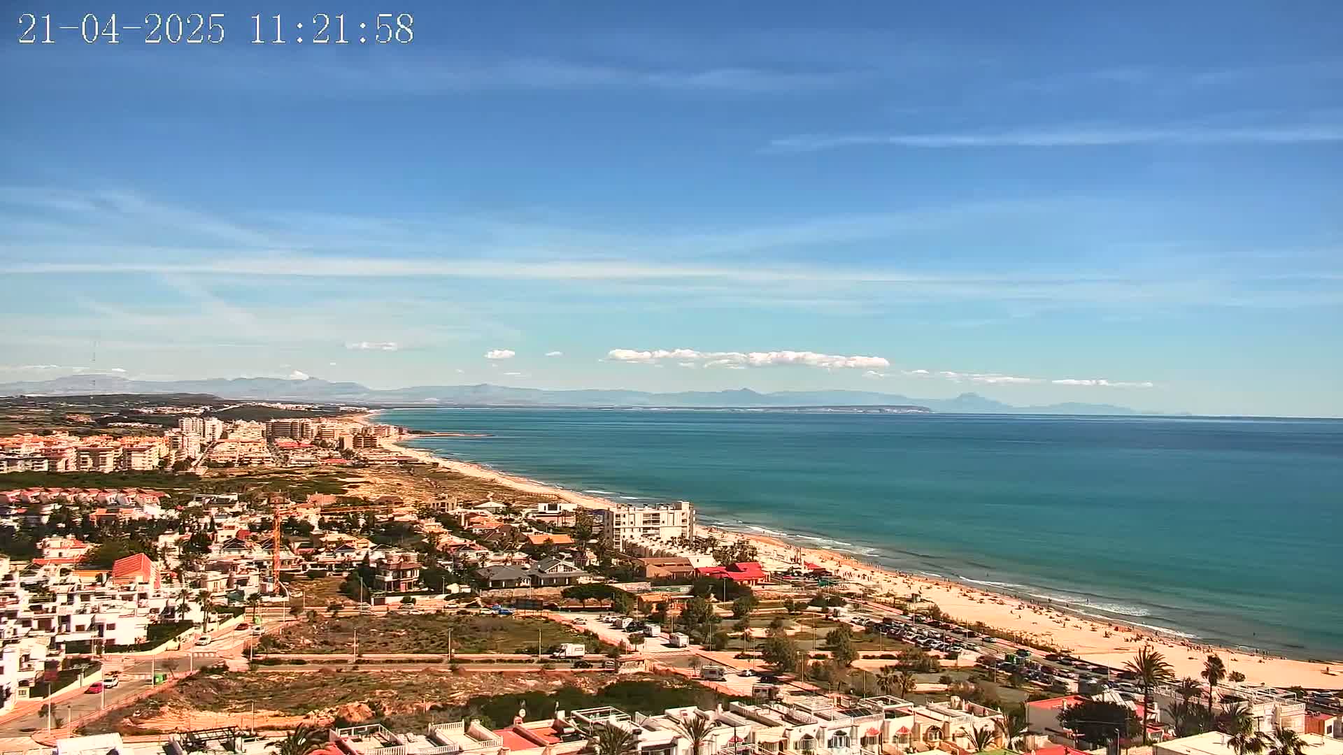 A coastal town sprawls along a sandy beach and turquoise ocean under a mostly clear blue sky.