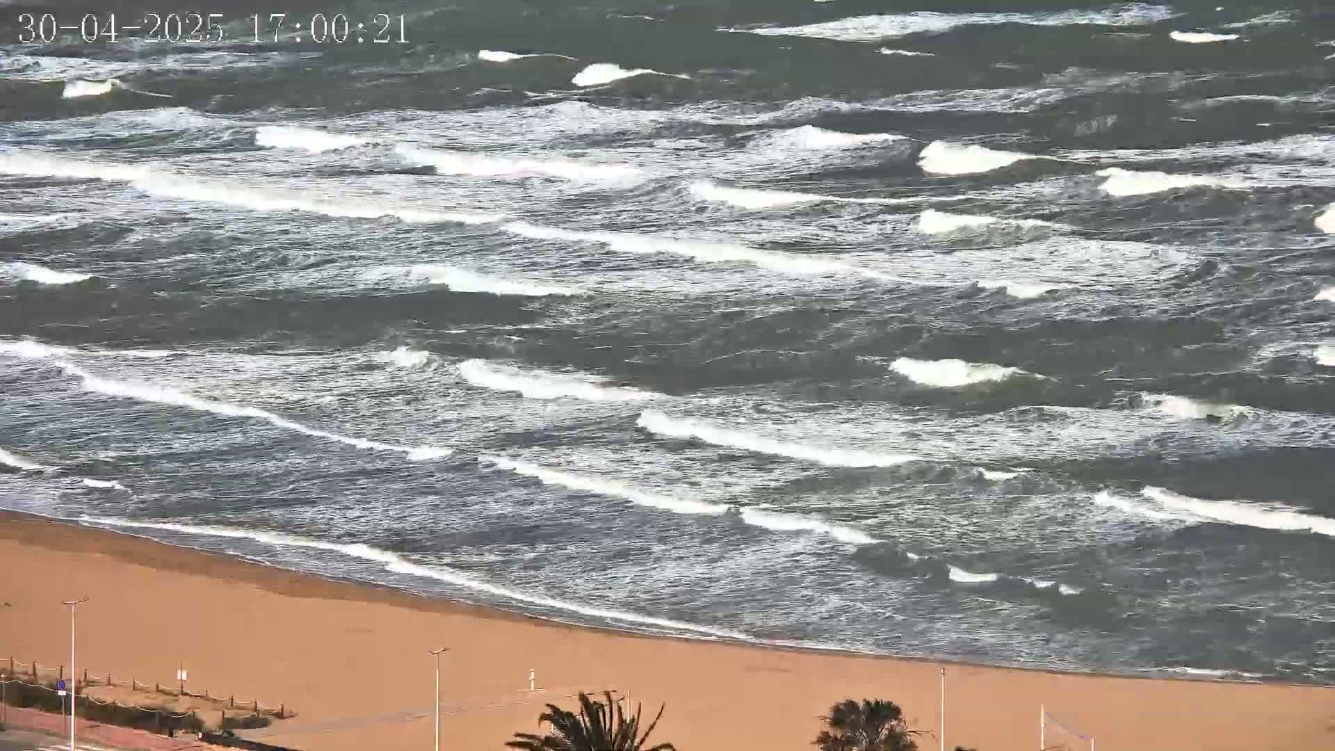A sandy beach is bordered by a choppy ocean with waves breaking on the shore under windy conditions.