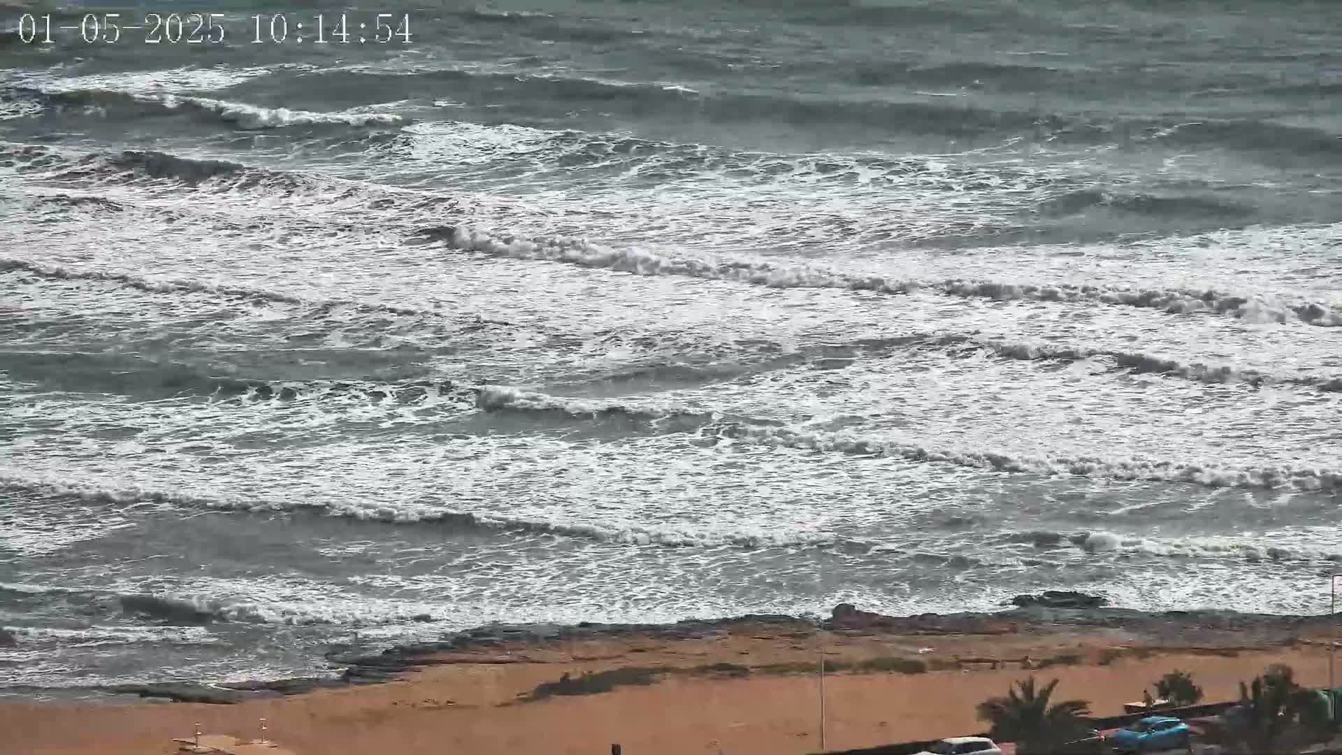 A view of a beach with choppy, gray-white waves crashing on a sandy shore under an overcast sky.